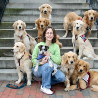 Deb Cunningham on steps with dogs around her and a dog in her arms