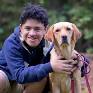 Boy in a dark blue sweatshirt with his arms around a yellow labrador dog