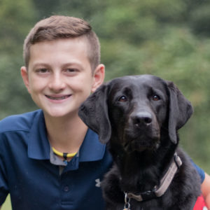 Boy in a navy blue polo with a black labrador dog