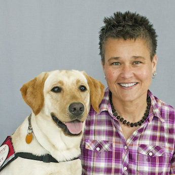 woman in a pink plaid shirt sitting next to a yellow lab dog