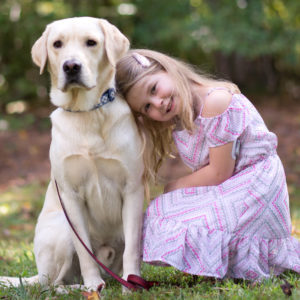 Young girl in a pink dress with a yellow labrador dog